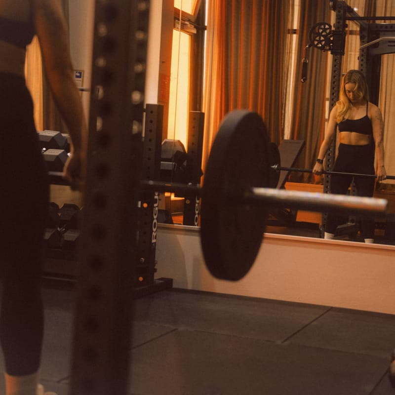 A loaded barbell in the Rogue rack at SHIO Private Gym, with the athlete reflected in the studio mirror